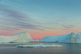 Iceberg mountains on Disko Bay, Greenland under red skies.