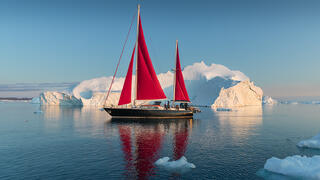 red sail boat and iceberg in Greenland 