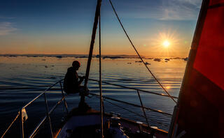 man on boat looking towards the midnight sun on Greenland waters