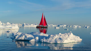 Photo of red sail boat and fragments of icebergs in Greenland