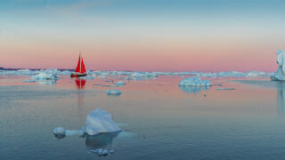 Red Sail boat on Greenland waters with midnight sun 