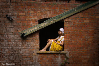 Female model in costume sitting in a window from an old pumping station.