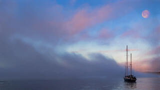Boat with no sails sailing into the sea mist on Disko Bay Greenland.