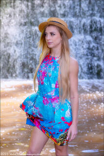 Female portrait in hat and summer dress with a waterfall in the background.  