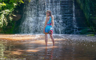 Female portrait in summer dress and hat, in waterfall.